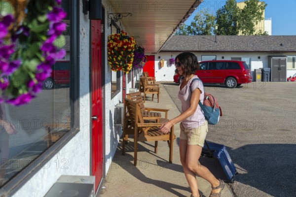 Female tourist is walking to her motel room pulling her wheeled suitcase, carrying a backpack and