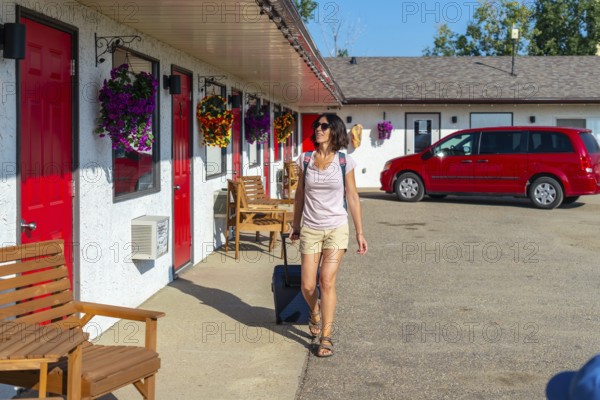 Female tourist pulling her luggage while strolling towards her room at a roadside motel, enjoying a