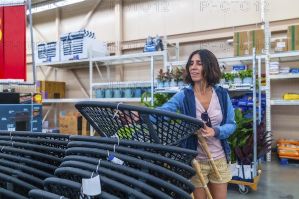 Smiling female customer selecting new outdoor furniture, picking up hanging egg chair in warehouse,