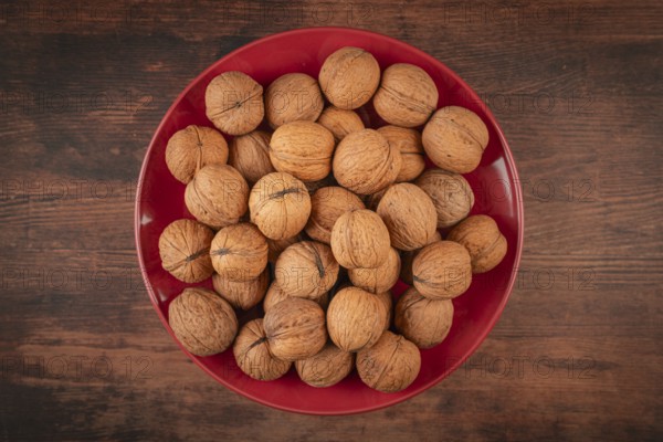 Red plate full of walnuts on a dark wooden table