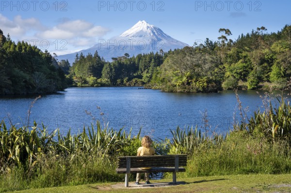 A woman sitting on a park bench at Lake Mangamahoe with views of Mount Taranaki. Egmont National