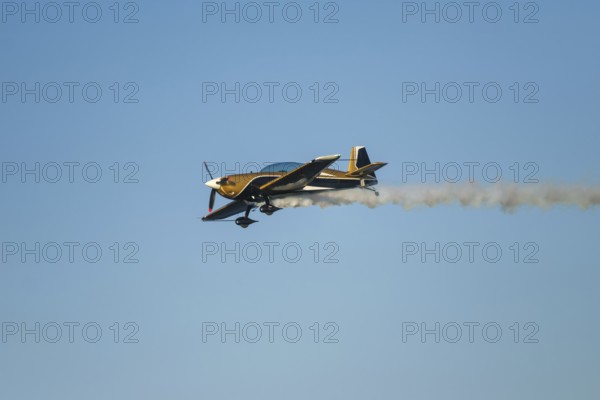 Golden stunt aerobatic plane performing stunts in blue sky with smoke trail. Concept of speed,