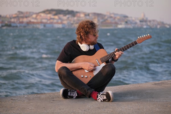Hipster street musician in black playing electric guitar in the street on sunset on embankment with