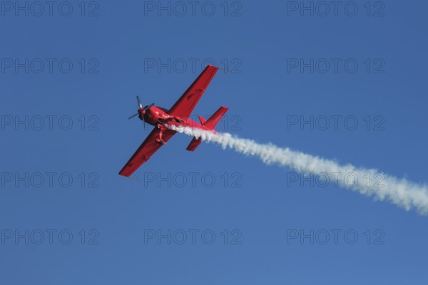 Red stunt aerobatic plane performing stunts in blue sky. Concept of speed, difficulty, precision,