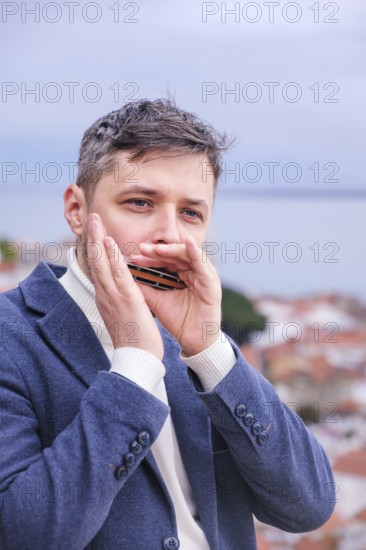 Man musician in a blue blazer and white sweater playing blues on a harmonica with eyes closed,