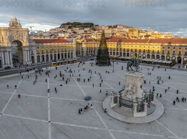 The scenic Praca do Comercio in Lisbon showcases a Christmas tree against the sunset sky,