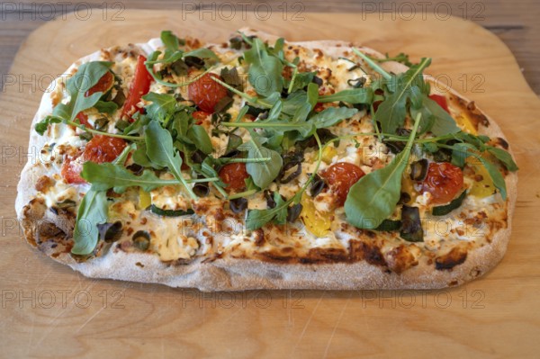 Pizza with goat cheese, tomatoes and arugula served on a wooden board, Ahrenshoop, DarÃŸ,