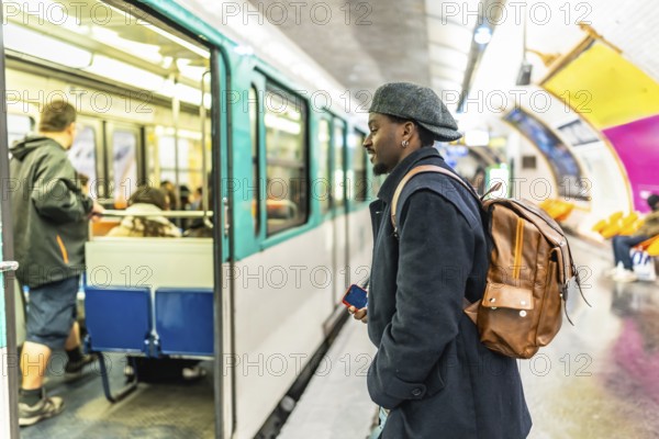 Young man stands on a bustling paris metro platform, looking toward an open train door as
