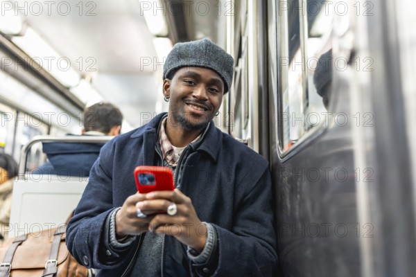 Young black man with a stylish hat smiling and looking at the camera while commuting on a subway