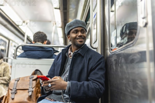 Young black man traveling on public transport, smiling and holding a smartphone, showcasing urban