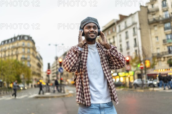 Young handsome black man walking a sunny european city street, smiling while listening to wireless