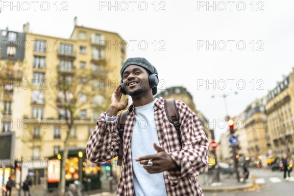 Young african man smiling and listening to music with headphones while walking in a bustling