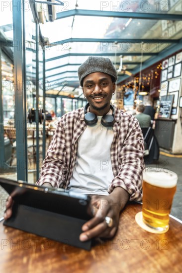 Young black man smiling, wearing headphones and a plaid shirt, looking at the camera while sitting