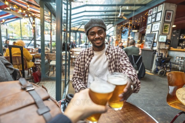 Young man smiling and clinking beer glasses with a friend in a casual pub, celebrating friendship,