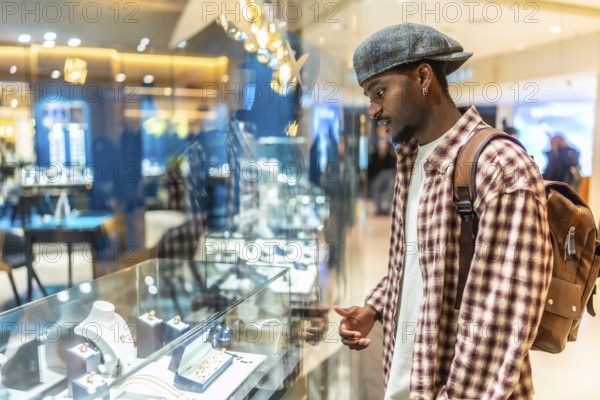 Young black man wearing a plaid shirt and cap intently looking at a display case filled with