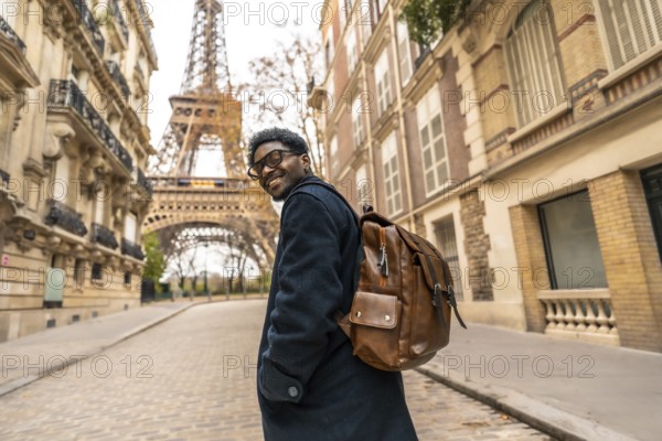 Young man smiling and turning back while exploring a historic street in paris, enjoying his leisure