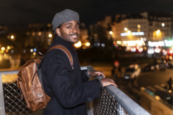 Young black man smiling while looking at the viewer, standing on a bridge overlooking the