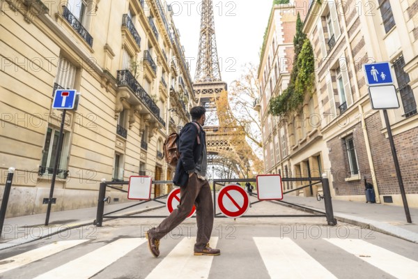 Young man with a backpack walking across a parisian crosswalk, historic buildings and the eiffel