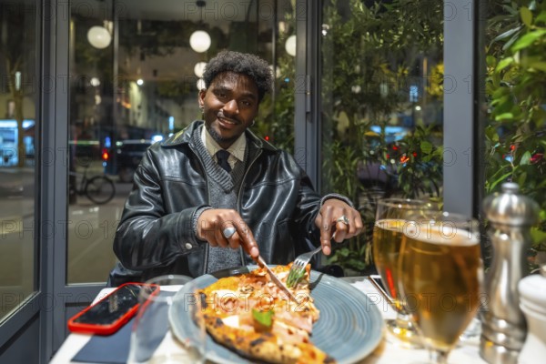 Young man smiling and cutting a delicious pizza slice with a knife and fork, enjoying a relaxing