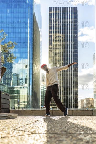 Young man with a red beanie striking a dynamic pose while dancing in an urban cityscape, backlit by