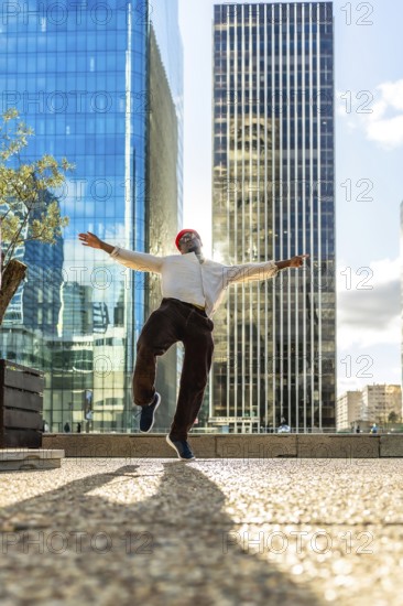 Young black man jumps with arms wide, celebrating joy and freedom against modern skyscrapers and