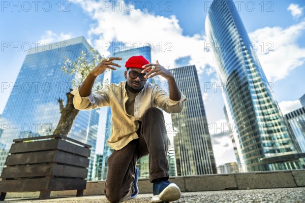 Young man wearing a red beanie and glasses, posing with hands raised in a low angle shot,