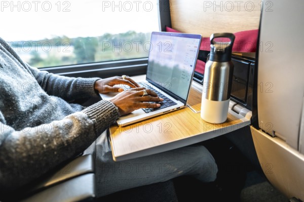 Man typing on a laptop computer while traveling by train, using the fold down tray table as a