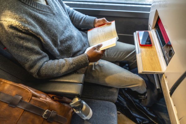 Black man enjoying a book while traveling by train, reflecting concepts of leisure, modern