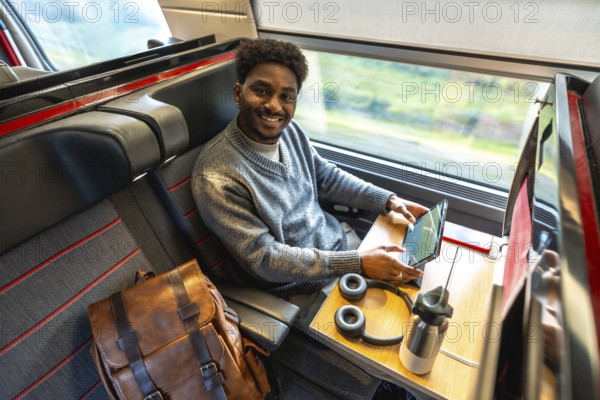 Young african american man traveling in a modern train, smiling and looking at the camera while
