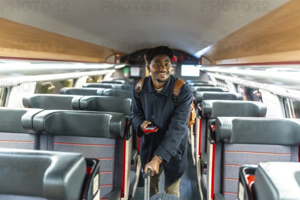 Young black man confidently walking through a train carriage, holding luggage and a mobile phone,