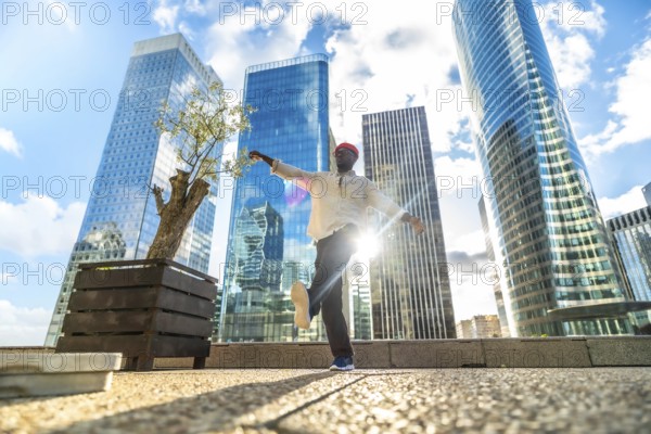 African american man dancing joyfully in a modern city square, arms outstretched against towering