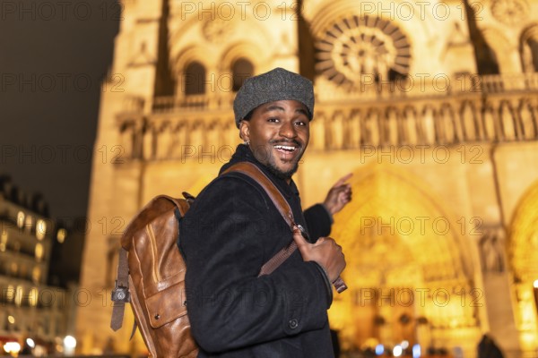 Joyful african american man with a backpack smiling and pointing, experiencing a nighttime tour of