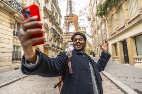 Young black man tourist smiling and recording a video selfie on his phone, waving hand, standing on