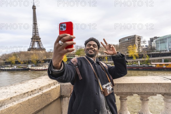 Young man smiling and making a peace sign while taking a selfie with a smartphone, capturing his