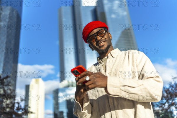 Young black man standing outdoors in a vibrant urban environment, smiling at the camera while