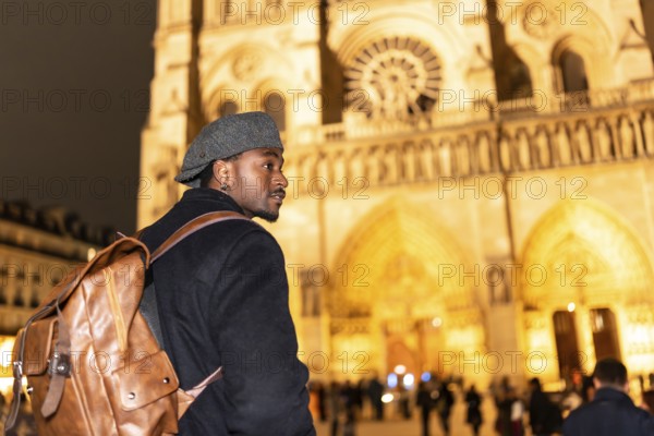 Young black man with a backpack and flat cap looking out while walking in front of notre dame