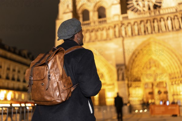 Solo man wearing a stylish cap and backpack, walking as a tourist during the night and looking at