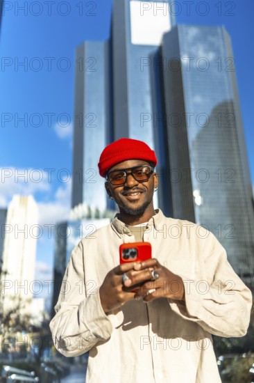 Stylish young black man wearing a red beanie and sunglasses, holding a bright red smartphone and