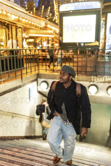 Young man wearing a beret, coat, and backpack ascending metro stairs in the vibrant urban