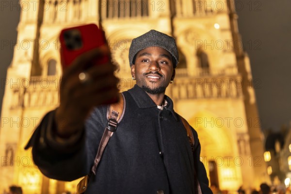 Young black man with a backpack smiling and taking a selfie with his smartphone in front of the