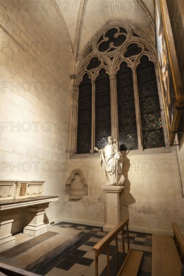 Gothic chapel interior featuring a statue of a saint, an arched window with detailed tracery, and