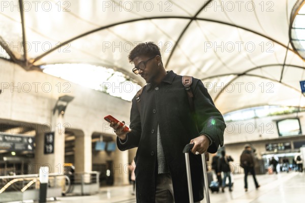 Indian businessman standing in a modern train station or airport terminal, looking down at his