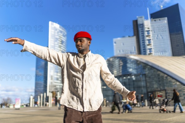 Black man wearing a red beanie and light shirt expressing creativity through dancing, arms spread