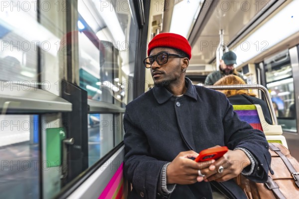 Stylish young black man wearing a red beanie and glasses sitting on a public transport train,