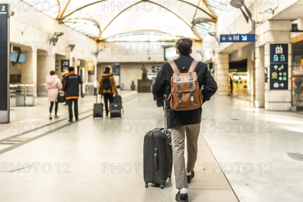 Businessman walking through a modern train station, pulling a suitcase and wearing a backpack,