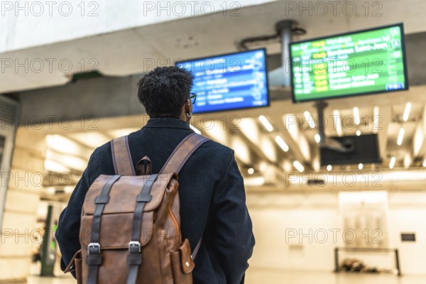 Man with a backpack standing at a train station, looking at the departure boards, preparing for a