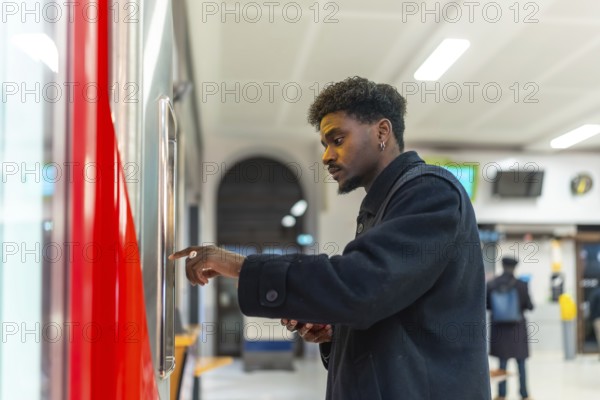 Young black man standing at a ticket machine in a modern train station, purchasing a ticket for his