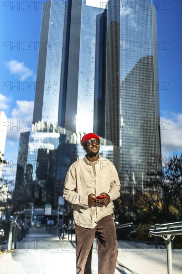 Young black man standing confidently in a modern city setting, wearing stylish casual attire and a