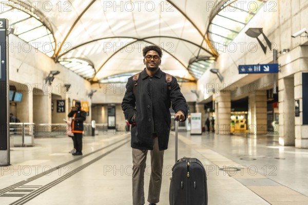 Young businessman standing on a modern train platform, smiling confidently with suitcase and
