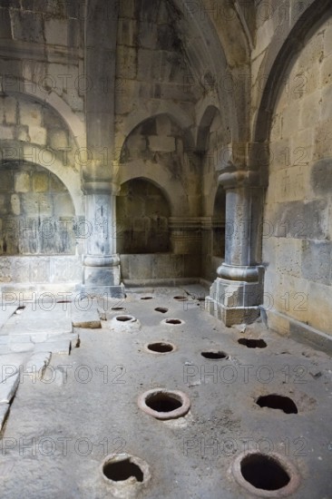 Stone room with large floor holes and massive pillars surrounded by weathered walls, Haghpat